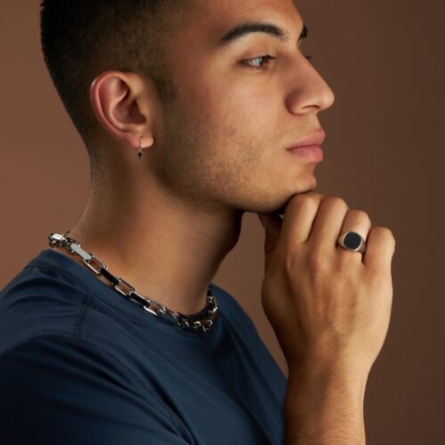 Side shot of a Hispanic male model wearing ring, ear ring and necklace for jewelry photography on a brown background.
